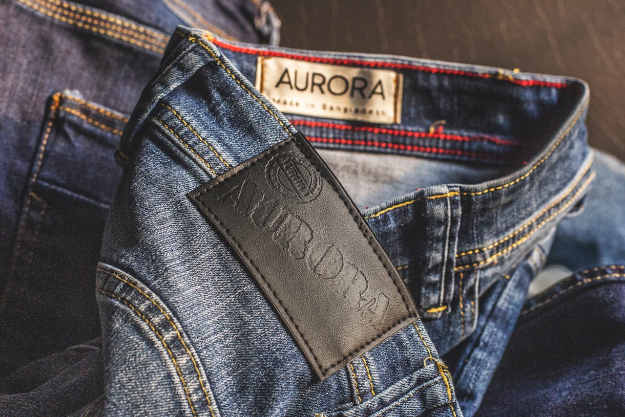 Home Close-up of blue denim jeans showcasing Aurora label, made in Bangladesh.